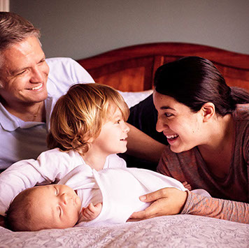 A Family lounging on a bed smiling at each other.